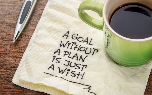 Green mug of coffee with a napkin that says, "A goal without a plan is just a wish."